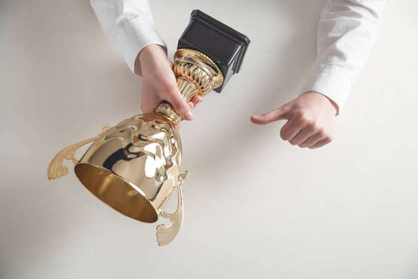  Χέρια που κρατούν χρυσό τρόπαιο στο λευκό γραφείο. Επιχειρήσεις, επιτυχία - Φωτογραφία, εικόνα