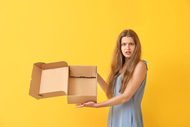 Mujer disgustada con caja de cartón vacía sobre fondo de color
 - Foto, Imagen