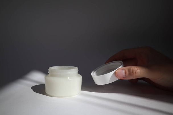 male hand opens White plastic tube with round cap on white background with shadows. Front view for your design. facial cosmetic products. Spa concept. Beauty blogger, salon treatments concept.  - 写真・画像