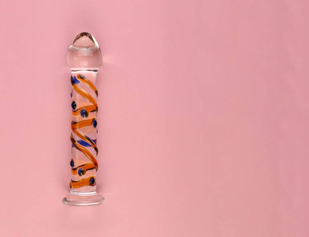 Mooie gelijkmatig verlichte glazen dildo op een effen roze achtergrond met kopieerruimte. - Foto, afbeelding