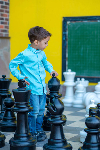 Ένα μικρό αγόρι που παίζει στο εξωτερικό σκάκι σε μια σκακιέρα με μεγάλο PI - Φωτογραφία, εικόνα