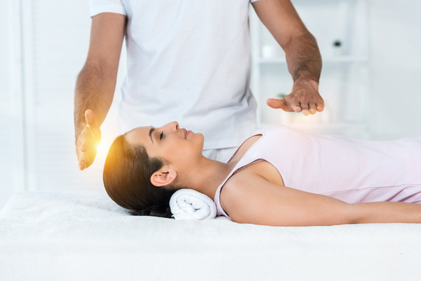vue recadrée du guérisseur mettant les mains au-dessus du corps de la femme attrayante avec les yeux fermés couché sur la table de massage
 - Photo, image