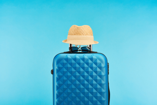 blue colorful travel bag with sunglasses and straw hat isolated on blue - Photo, Image
