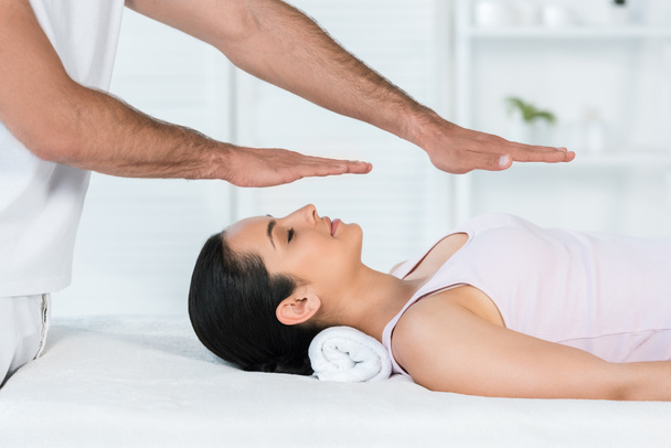 vue recadrée du guérisseur mettant les mains au-dessus du corps de la femme avec les yeux fermés couché sur la table de massage
 - Photo, image