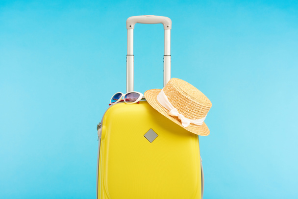 saco de viagem colorido amarelo com chapéu de palha e óculos de sol isolados em azul
 - Foto, Imagem