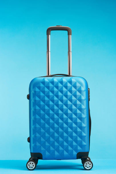 blue travel bag with handle on wheels on blue background - Foto, afbeelding