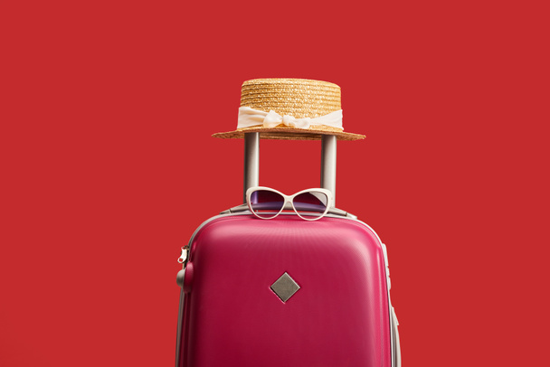 červený barevný cestovní vak se slaměnou pokrývkou a slunečními brýlemi, izolované na červenou  - Fotografie, Obrázek