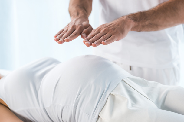 妊娠中の女性のおなかの上に手を置くヒーラーのトリミングビュー  - 写真・画像