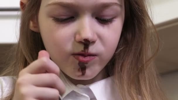 Μικρό κορίτσι με βρώμικο πρόσωπο τρώει πουτίγκα σοκολάτας κοντά - Πλάνα, βίντεο