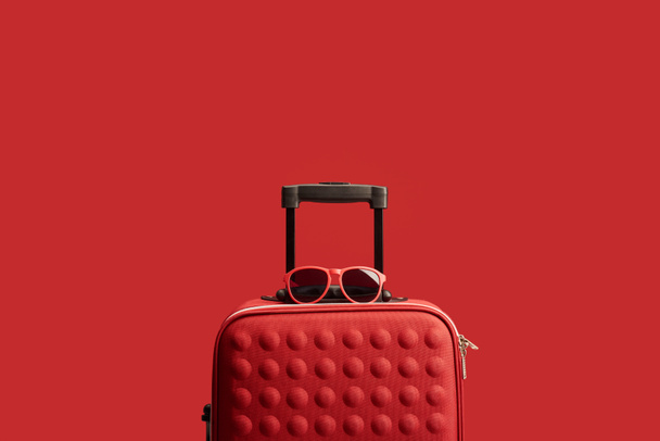 red colorful textured travel bag with sunglasses isolated on red  - Foto, Bild