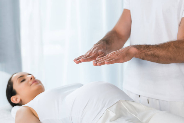 selective focus of man healing brunette pregnant woman lying on massage table  - Foto, Imagem