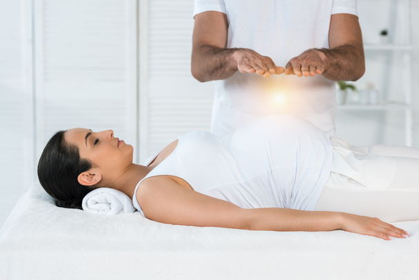 bijgesneden weergave van man genezing aantrekkelijke zwangere vrouw liggend op massagetafel  - Foto, afbeelding
