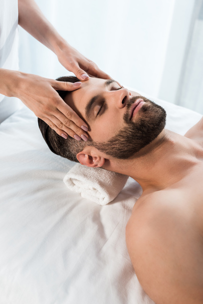 cropped view of masseur doing massage to handsome man with closed eyes - Fotografie, Obrázek