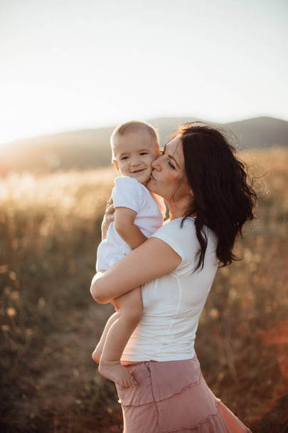Macierzyństwo-młoda matka przytulanie jej szczęśliwego dziecka w polach o zachodzie słońca. - Zdjęcie, obraz