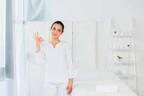 cheerful brunette woman showing ok sign in spa center  - Photo, Image
