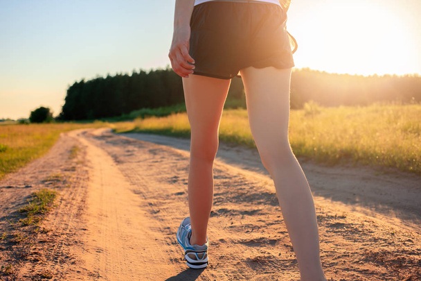 Bieganie koncepcja ćwiczeń, fitness i zdrowego stylu życia. Sportowiec biegacz stopy biegną na polnej drodze przez pole w wschodzie słońca. - Zdjęcie, obraz