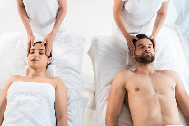 vista recortada de masajistas haciendo masaje a hombre y mujer con los ojos cerrados en el centro de spa
  - Foto, Imagen