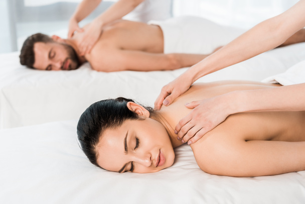 Selektywny fokus masażysta robi masaż dla kobiety z zamkniętymi oczami w pobliżu człowieka w centrum spa  - Zdjęcie, obraz