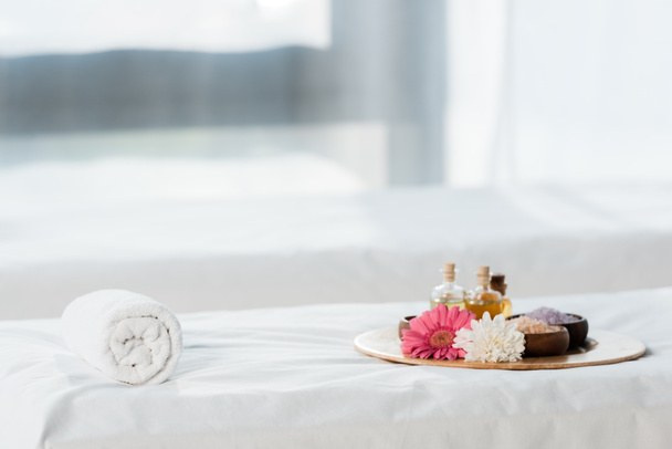 selective focus of tray with bottles of oil, bowls with sea salt and flowers in spa center  - Photo, Image