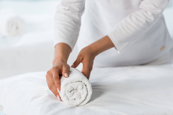 przycięte widok masażysta stojący w pobliżu stołu do masażu i trzymając ręcznik roll  - Zdjęcie, obraz