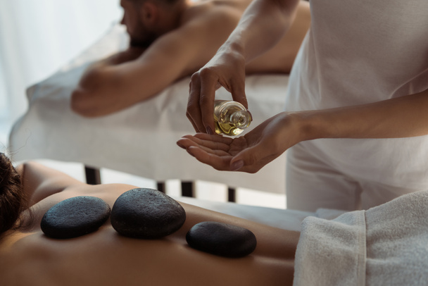 vista recortada de masajista celebración botella con aceite cerca de la mujer y el hombre en el centro de spa
  - Foto, imagen