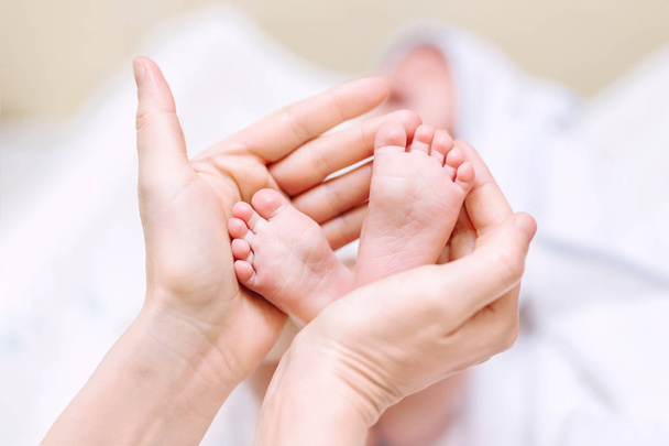Anya újszülött baba lábat tart a kezében. Anya vigyáz a csecsemőre fürdés után. A szülők gyermekgondozása. Gyermekek egészségügyi ellátása és boldog család - Fotó, kép