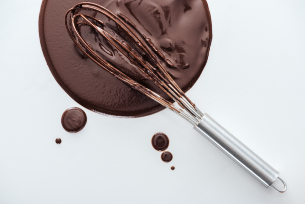 Top view of balloon whisk with circle of melted chocolate on white background  - Photo, Image