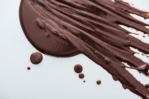 Draufsicht auf verschüttete dunkle Schokolade und Schokoladentropfen auf weißem Hintergrund - Foto, Bild