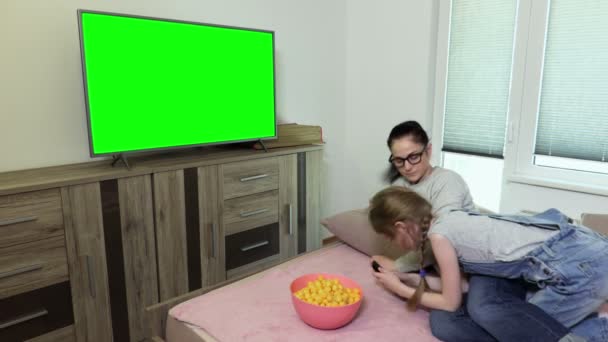 Tochter und Mutter mit Fernbedienung in der Nähe des Fernsehers mit grünem Bildschirm - Filmmaterial, Video