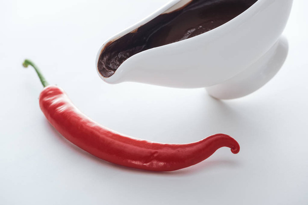 Vista de alto ángulo de chile y bote de salsa con chocolate derretido sobre fondo blanco
  - Foto, Imagen