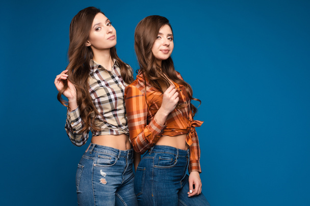 Twee slanke zusters in geruite shirts en jeans poseren - Foto, afbeelding