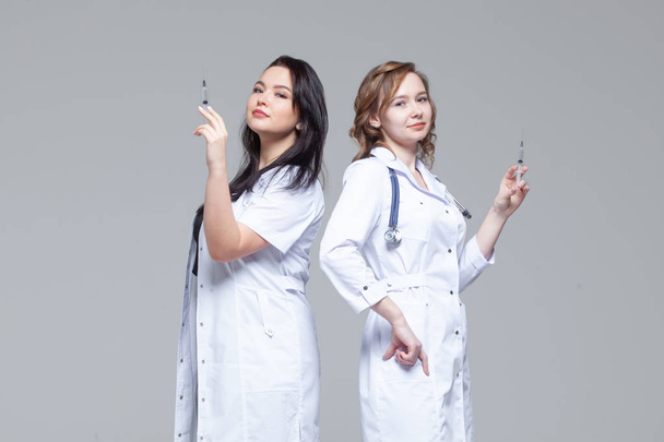 Two female doctors standing back-to-back hold ready-to-inject syringes - Photo, Image