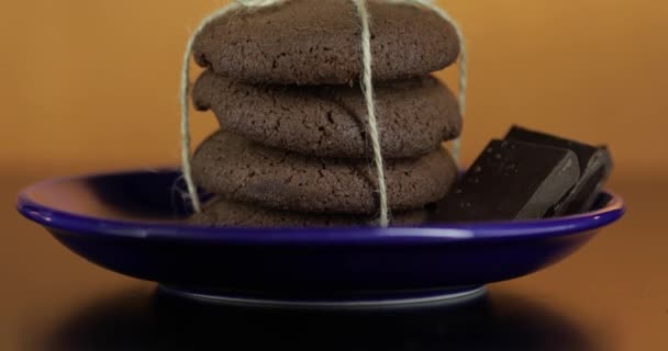 Νόστιμο φαίνεται μπισκότο σοκολάτας σε ένα μπλε πιάτο στη σκοτεινή επιφάνεια. Θερμό φόντο - Πλάνα, βίντεο