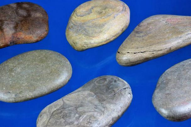 Sea stones of natural origin - the fragments of natural stones rolled by water on a blue background. Stones are used for Massage stone therapy, for treatment, for creative design - Photo, Image