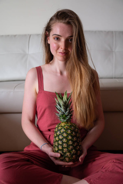 Young tired female sitting on floor with pineapple - Fotoğraf, Görsel