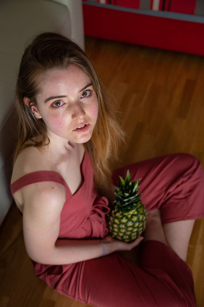 Young tired female sitting on floor with pineapple - Φωτογραφία, εικόνα