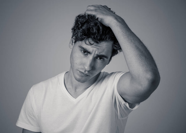 Young attractive stylish fashion man in his 20s looking sexy in casual clothes and dark curly hair posing against neutral background. Portrait of sweet and masculine model. People and Beauty concept. - 写真・画像