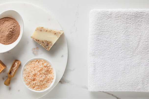 vista superior de polvo de arcilla, sal marina y jabón sobre una mesa de mármol cerca de una toalla de algodón blanco
 - Foto, imagen