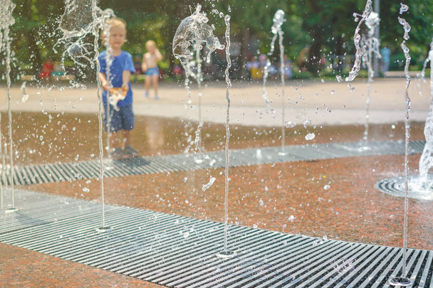 A boy playing with water in park fountain. Hot summer. Happy young boy has fun playing in water fountains  - Photo, Image