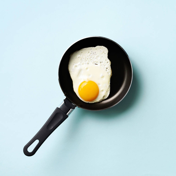 Creative food concept with fried egg on pan over blue background. Top view. Creative pattern in minimal style. Flat lay. Square crop - Foto, Imagem