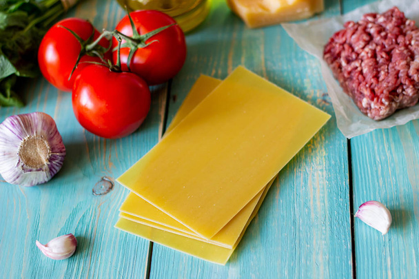 Lasagna, tomatoes, minced meat and other ingredients. Blue wooden background. Italian cuisine. - Photo, image