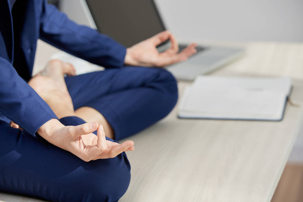 Cropped image of business lady sitting in lotus position on her office table - Zdjęcie, obraz