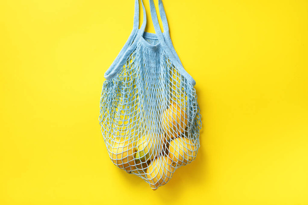 Mesh shopping bag with lemons on yellow paper background. Flat lay, top view. Zero waste, plastic free concept. Healthy clean eating diet and detox. Summer fruits - Fotoğraf, Görsel