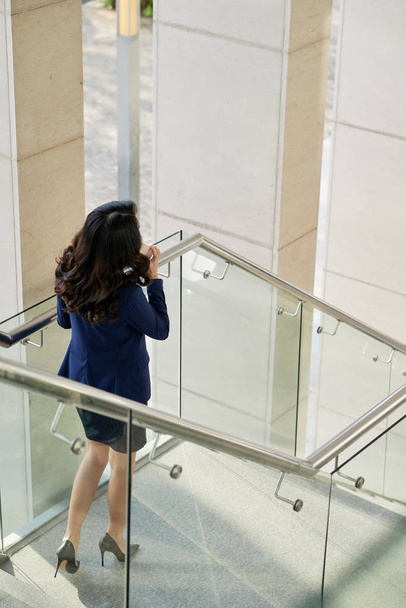 Vista trasera de la dama de negocios llamando por teléfono cuando está de pie en las escaleras
 - Foto, Imagen