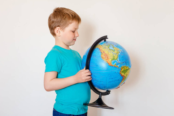 seven-year-old Caucasian boy holding a large globe - Фото, изображение