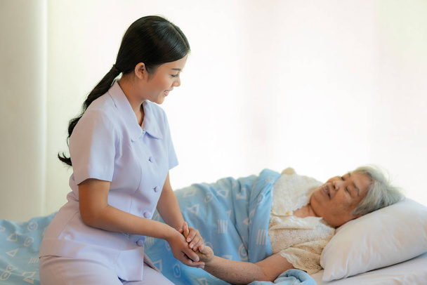 Nővér, ül egy kórházi ágyon mellett egy idősebb nő, segítve a h - Fotó, kép