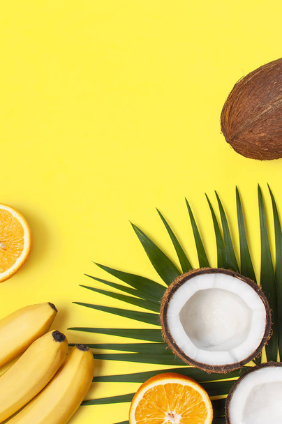 Summer tropical composition. Green tropical leaves of palm trees and monstera, coconut, orange, bananas on bright yellow background. Flat lay, top view, copy space. Creative background food, fruit - Foto, Imagem