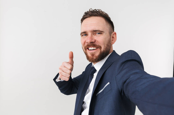 Handsome businessman posing isolated over white wall background showing thumbs up and take selfie. - Foto, Imagen