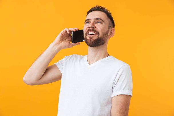 Щасливий чоловік позує ізольовано на жовтому фоні стіни, розмовляючи по телефону
. - Фото, зображення