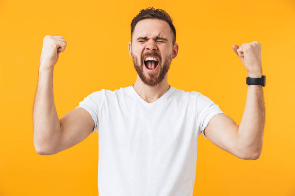 Man posing isolated over yellow wall background make winner gesture. - Фото, изображение